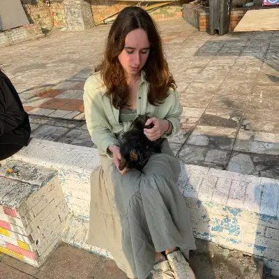 Eliska sitting on a low wall in the sunshine, holding a small black puppy on her lap